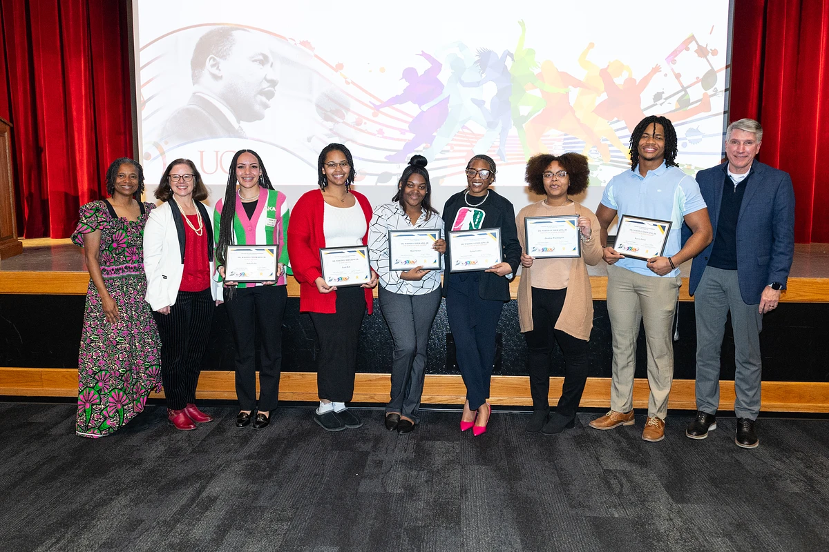 A group of people stand on a stage holding certificates with a colorful backdrop featuring an image of Martin Luther King Jr.